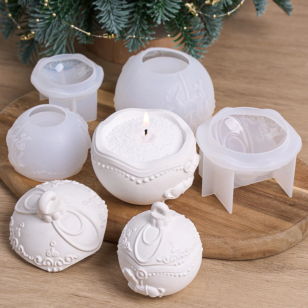 A set of white ceramic candle holders with ornate embossed floral and scroll designs, displayed on a wooden board with one candle lit and holiday greenery in the background.