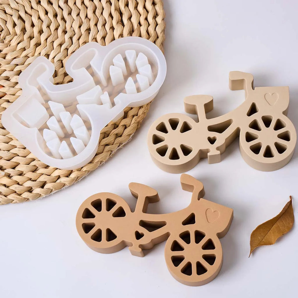 Three bicycle-shaped decorative items arranged on a white surface with a woven mat: one translucent white item and two natural wood items, all shown clearly with no people or real environment.