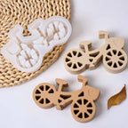 Three bicycle-shaped decorative items arranged on a white surface with a woven mat: one translucent white item and two natural wood items, all shown clearly with no people or real environment.