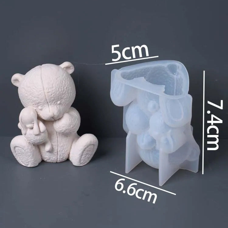 A translucent silicone mold shaped like a teddy bear holding a small doll, shown next to a white unmolded teddy bear figure for scale. White text overlays indicate dimensions of the mold (5cm, 6.