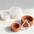 Three ribbed circular jewelry boxes in terracotta and white, with one box open and displaying a white pearl strand, on a clean white background.