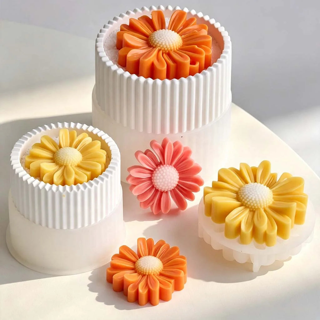 Four flower-shaped molded items in orange, yellow, and pink displayed on white ribbed cylindrical molds against a clean white background.